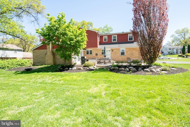 back of house featuring a lawn, brick siding, and a patio area