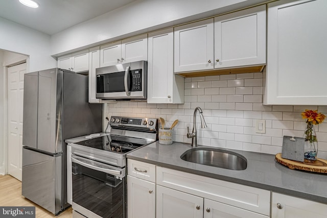 kitchen featuring a sink, dark countertops, stainless steel appliances, and white cabinetry