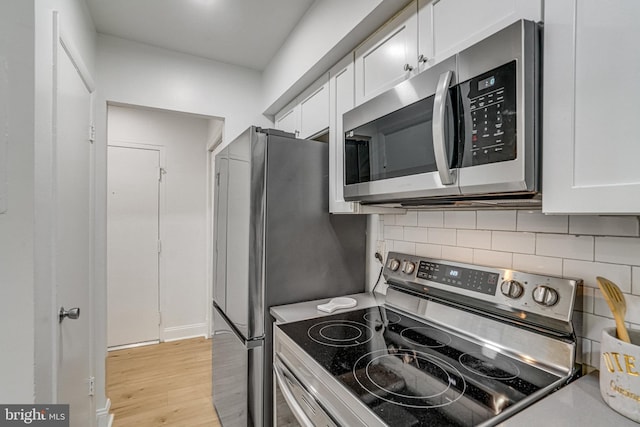 kitchen featuring decorative backsplash, white cabinetry, light wood finished floors, and stainless steel appliances
