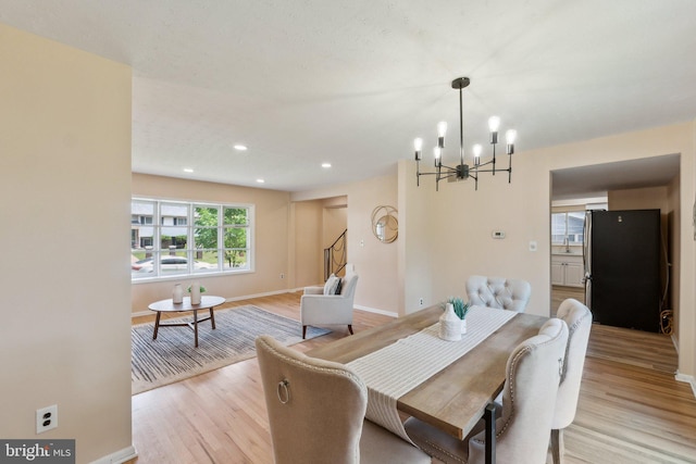 dining area featuring stairway, light wood finished floors, a notable chandelier, and baseboards