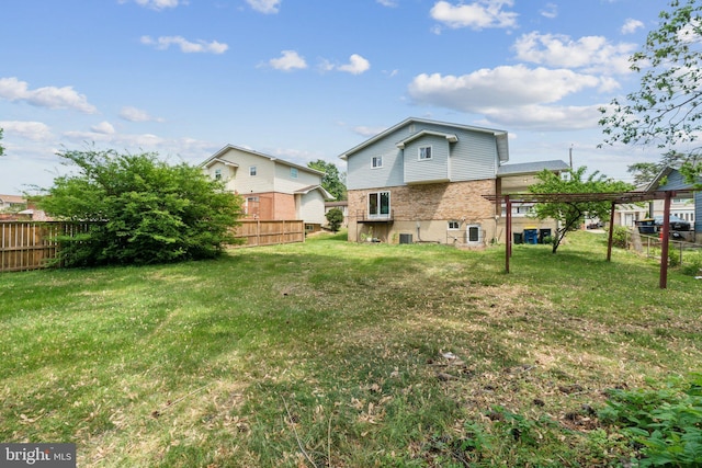 back of house with a lawn, brick siding, fence, and a carport