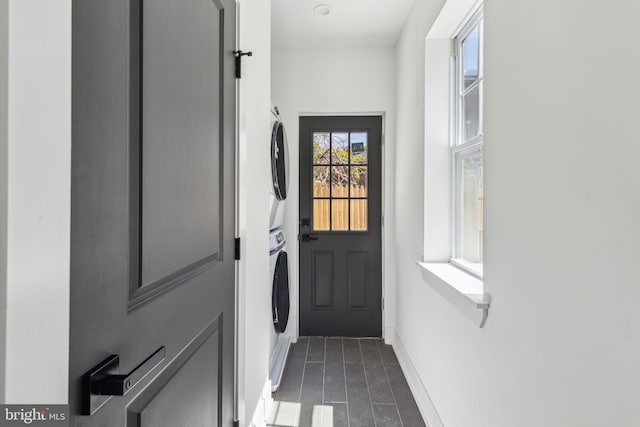 entryway featuring stacked washer and dryer, dark tile patterned flooring, and baseboards