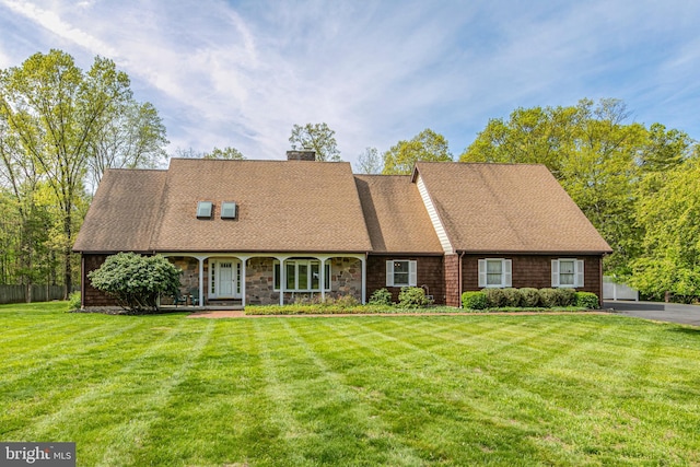 cape cod house with a front lawn, a chimney, roof with shingles, and covered porch