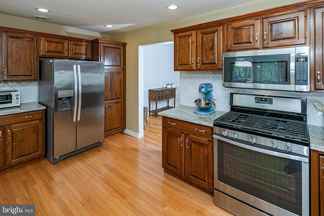 kitchen featuring appliances with stainless steel finishes, backsplash, light wood-type flooring, light stone counters, and recessed lighting