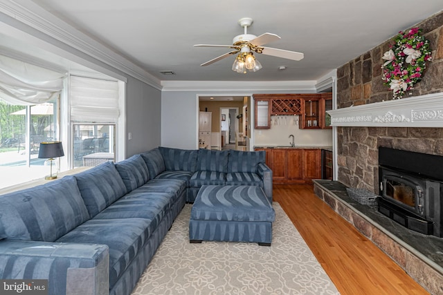 living room with light wood-style floors, a wood stove, ceiling fan, ornamental molding, and bar