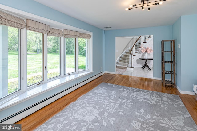 empty room featuring baseboard heating, stairs, baseboards, and wood finished floors