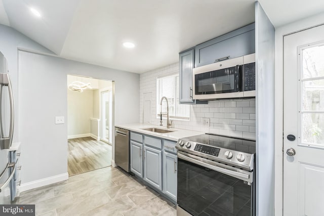 kitchen featuring stainless steel appliances, a sink, decorative backsplash, gray cabinets, and light countertops