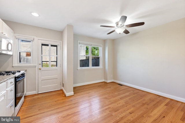 kitchen with ceiling fan, light wood-style floors, range with gas stovetop, white cabinetry, and baseboards
