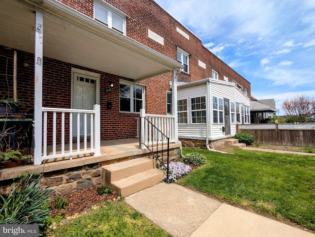entrance to property with a lawn, fence, a porch, and brick siding