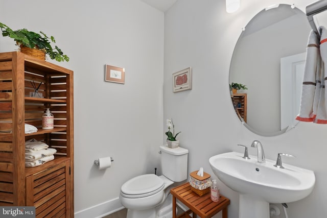 half bath with toilet, baseboards, and a sink