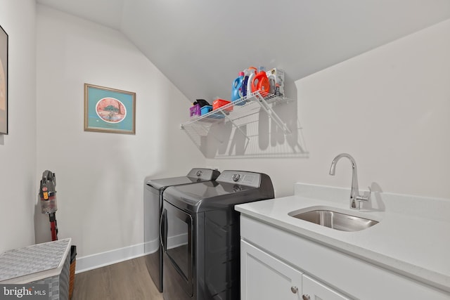 clothes washing area featuring a sink, baseboards, wood finished floors, cabinet space, and washer and dryer