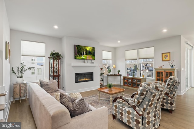 living area with a glass covered fireplace, plenty of natural light, and wood finished floors