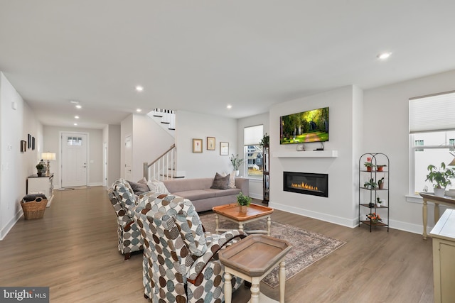 living room with plenty of natural light, a glass covered fireplace, recessed lighting, wood finished floors, and stairway