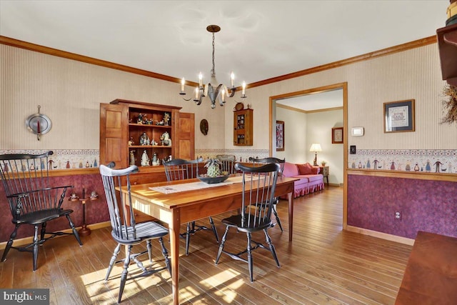 dining room with a notable chandelier, baseboards, ornamental molding, wallpapered walls, and hardwood / wood-style flooring