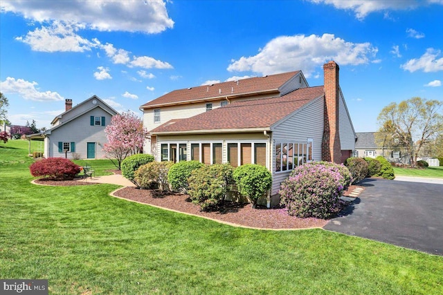 rear view of property featuring a lawn, roof with shingles, and a chimney