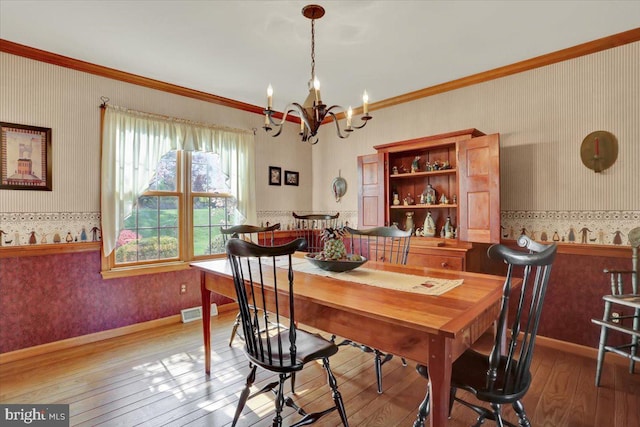 dining area featuring a notable chandelier, wallpapered walls, hardwood / wood-style flooring, and visible vents