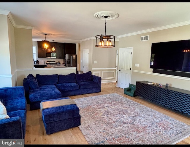 living room featuring light wood-style floors, ornamental molding, a chandelier, and visible vents