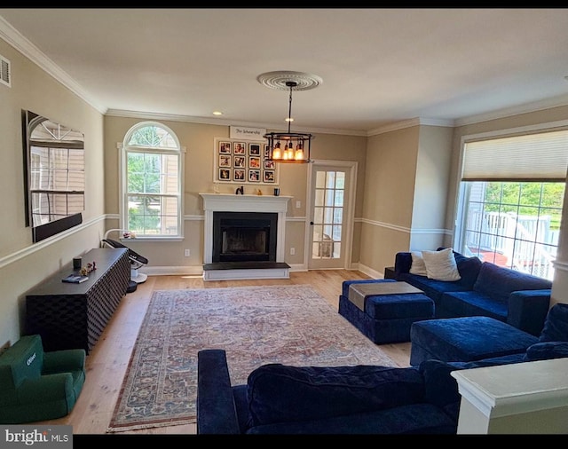 living area with baseboards, a fireplace with raised hearth, an inviting chandelier, ornamental molding, and light wood-style flooring