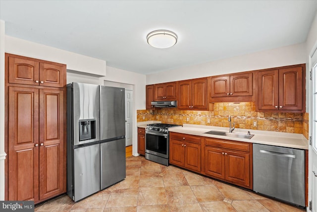 kitchen featuring under cabinet range hood, light countertops, a sink, decorative backsplash, and appliances with stainless steel finishes