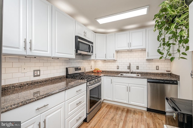 5511 Gwyn Pl, Alexandria, VA 22312 - kitchen with stainless steel appliances, a sink, white cabinets, tasteful backsplash, and light wood-style flooring