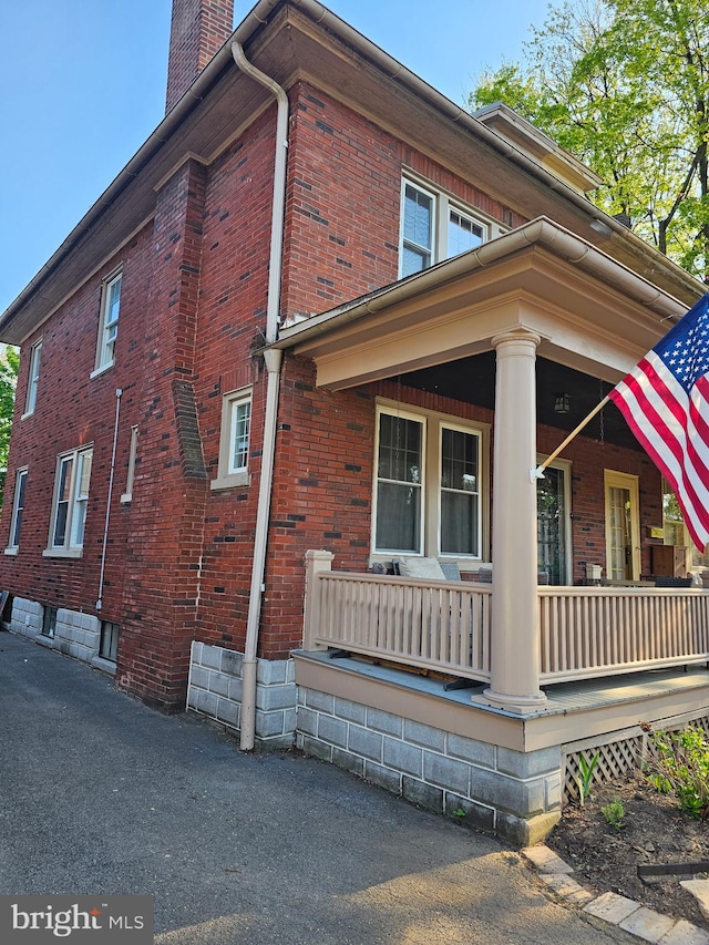 view of side of property with covered porch, brick siding, and a chimney