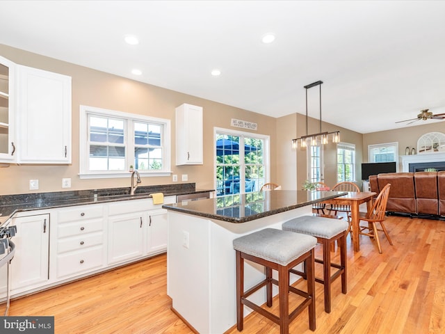 kitchen with a breakfast bar, a center island, white cabinets, a sink, and light wood finished floors