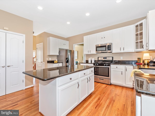 kitchen featuring a kitchen island, dark stone countertops, white cabinets, light wood finished floors, and stainless steel appliances