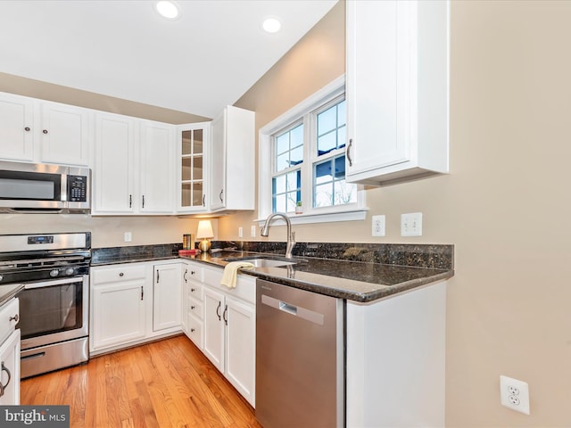 kitchen featuring dark stone countertops, white cabinetry, a sink, light wood finished floors, and appliances with stainless steel finishes