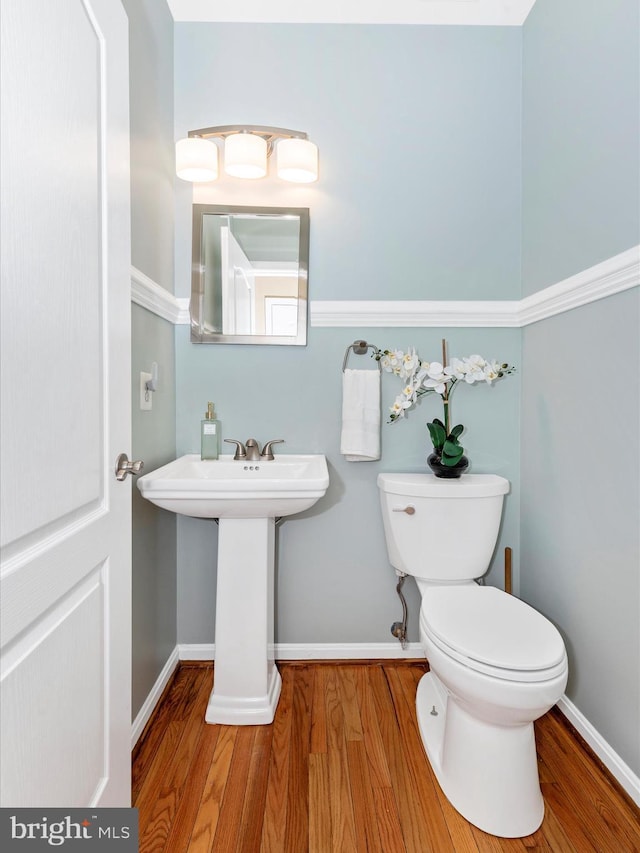 half bath with baseboards, toilet, and wood finished floors