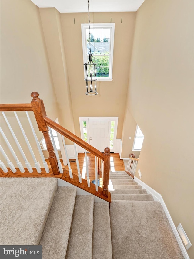 stairs with baseboards, a towering ceiling, a notable chandelier, and a healthy amount of sunlight