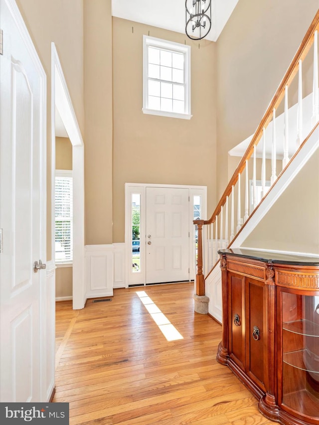 entrance foyer featuring stairs, light wood-style floors, an inviting chandelier, and a towering ceiling