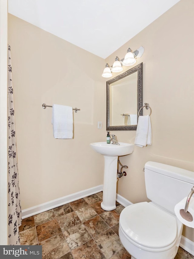 bathroom featuring toilet, baseboards, and stone finish floor