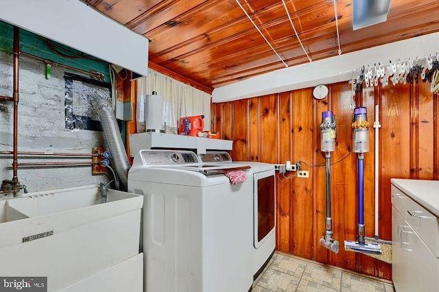 laundry room with wood ceiling, laundry area, independent washer and dryer, a sink, and wooden walls