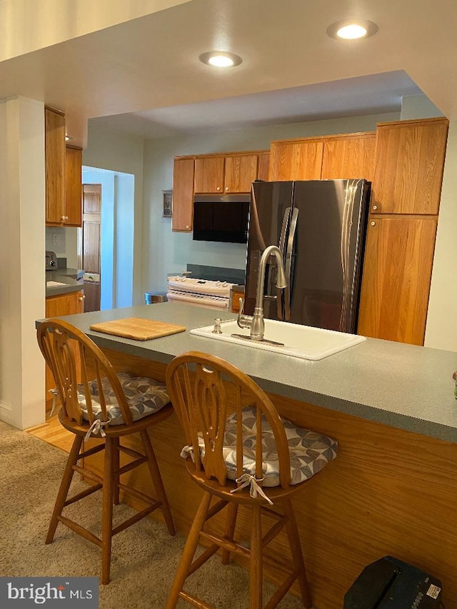 kitchen featuring a breakfast bar area, light colored carpet, appliances with stainless steel finishes, brown cabinets, and a sink