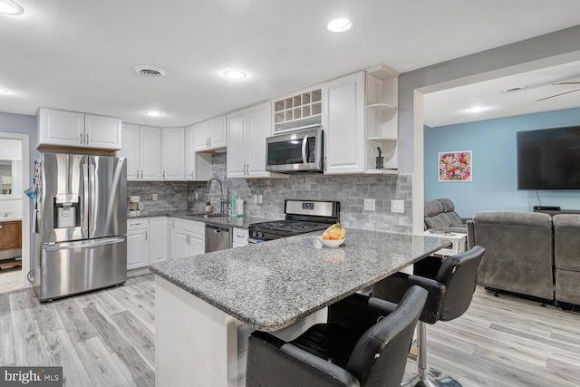 kitchen with light wood-style flooring, light stone counters, stainless steel appliances, a sink, and a peninsula