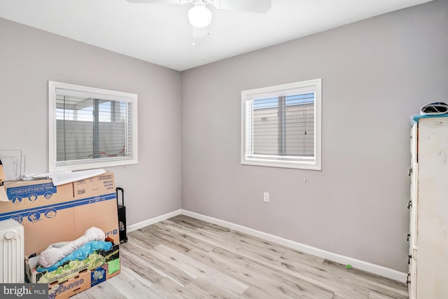 unfurnished bedroom featuring radiator heating unit, light wood-type flooring, baseboards, and multiple windows