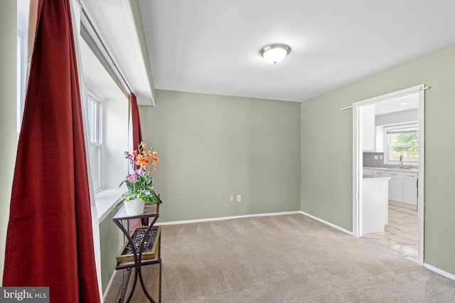 spare room with baseboards, a sink, and light colored carpet