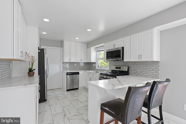 kitchen featuring a peninsula, white cabinets, backsplash, appliances with stainless steel finishes, and marble finish floor