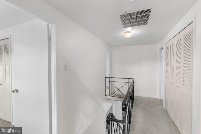 corridor featuring an upstairs landing, visible vents, and carpet floors