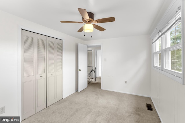 unfurnished bedroom featuring a closet, light colored carpet, visible vents, a ceiling fan, and baseboards