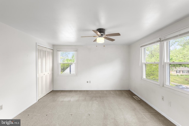 carpeted empty room with baseboards, a wealth of natural light, ceiling fan, and visible vents