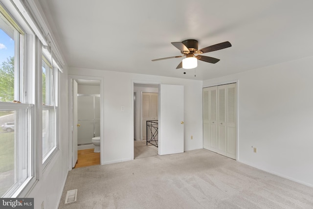 unfurnished bedroom with a closet, carpet floors, visible vents, ceiling fan, and ensuite bath