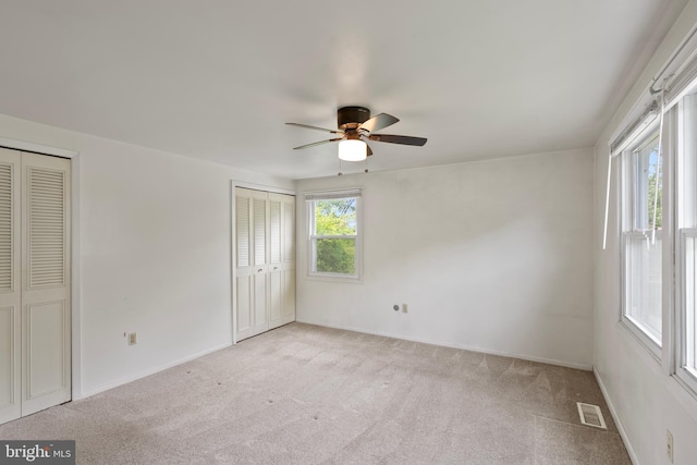 unfurnished bedroom with carpet floors, two closets, visible vents, baseboards, and ceiling fan