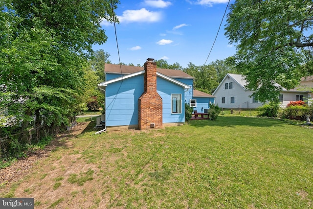 rear view of property with a lawn, a chimney, and fence