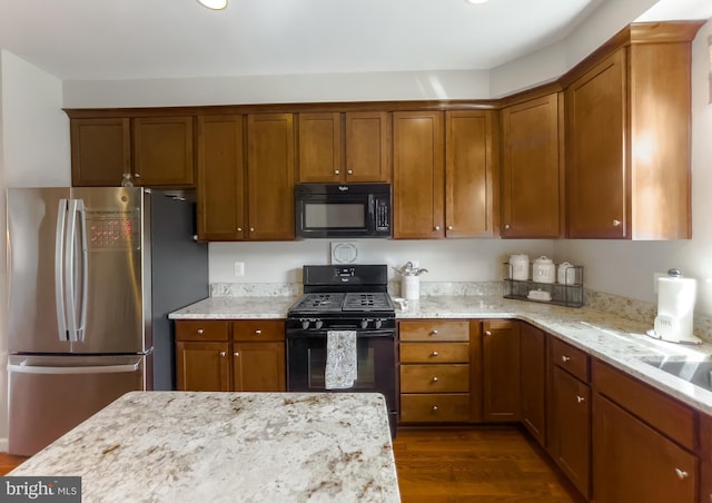 kitchen with brown cabinetry, dark wood-style flooring, and black appliances