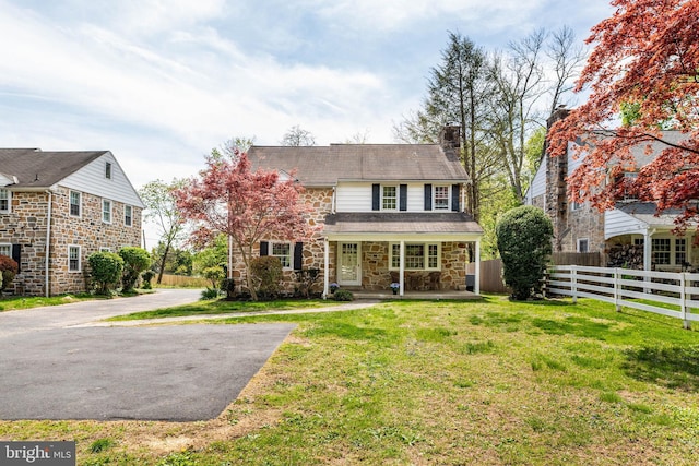 view of front facade featuring fence, a front yard, stone siding, a chimney, and a porch