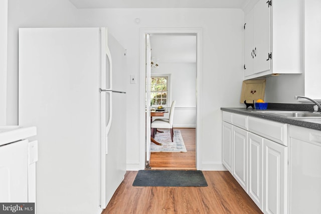 kitchen featuring freestanding refrigerator, dark countertops, white cabinets, a sink, and light wood-style flooring