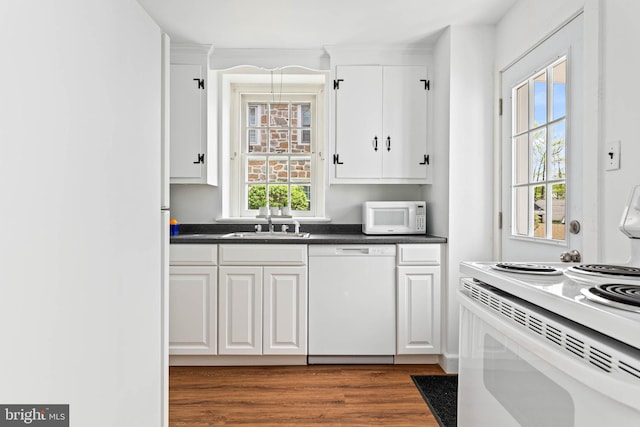 kitchen featuring white cabinets, dark countertops, a sink, white appliances, and dark wood finished floors