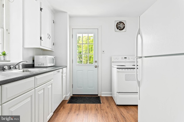 kitchen featuring white cabinets, dark countertops, a sink, white appliances, and light wood-type flooring