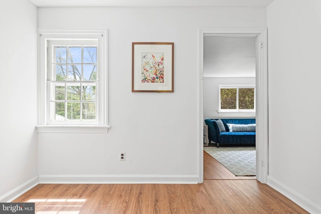 hall featuring baseboards, a healthy amount of sunlight, and wood finished floors